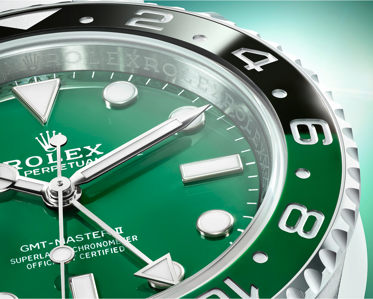 A sleek silver wristwatch with a black dial and bezel is displayed against a gradient background from teal to white.